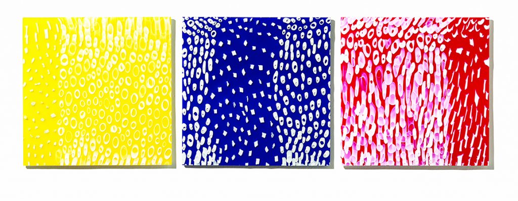 Three square glass panels in opaque red, yellow and blue with white patterns 