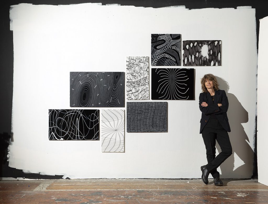 Nancy Callan leaning against wall next to installation of glass panels