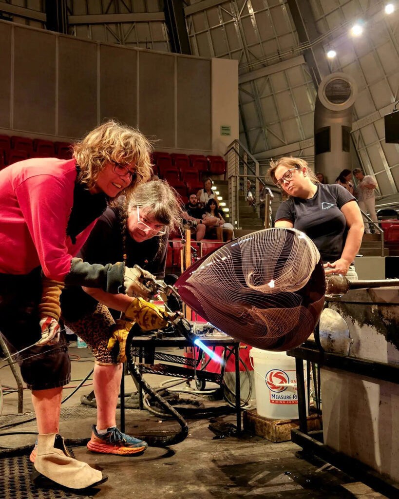 Nancy Callan at work with two female assistants and a large glass object on the pipe