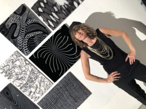 Photo of Nancy Callan with hands on hips and gold necklace in front of glass panel wall installation 