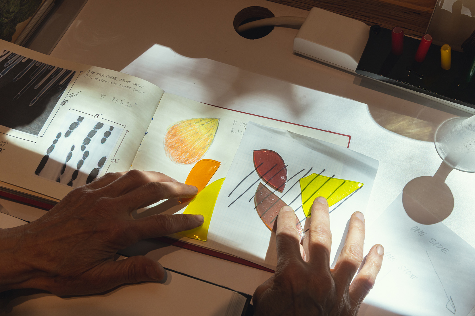 image of hands placing colored glass pieces in sunlight on desk