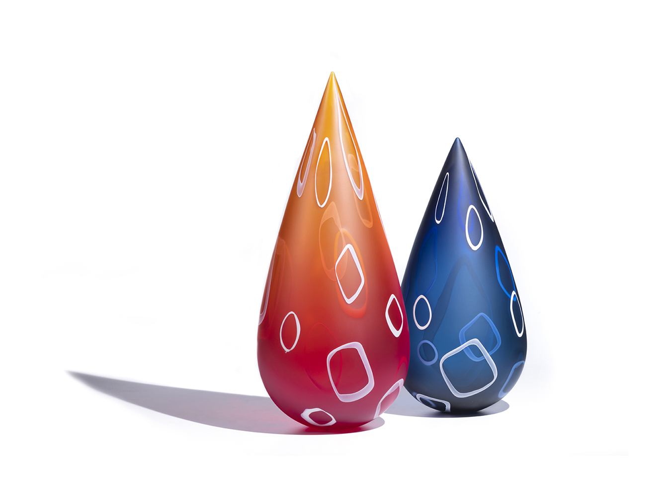 Two glass sculptures in tall teardrop shape, left is orange and right is blue