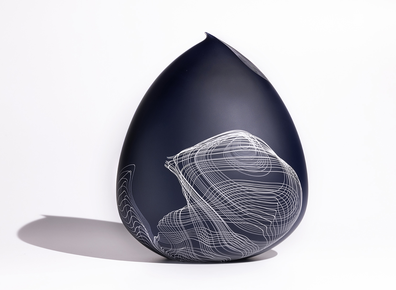 Deep blue glass sculpture with delicate twisting white lines, reverse side